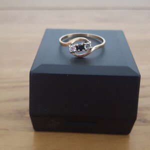 May include: A gold ring with a twisted band and three stones. The center stone is black and the two stones on either side are white.