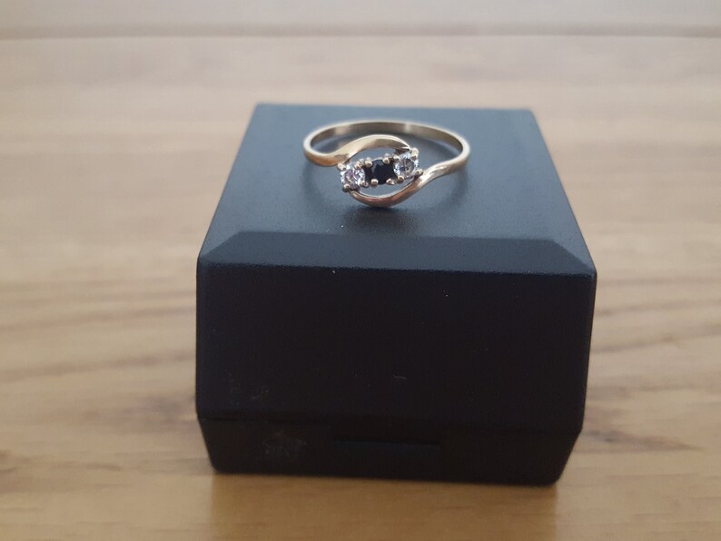 May include: A gold ring with a twisted band and three stones. The center stone is black and the two stones on either side are white.