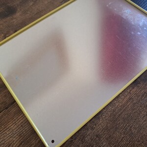 May include: A blank metal sign with a yellow border. The sign is made of a thin metal sheet and has a slightly textured surface.