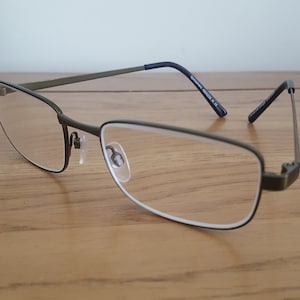 Op de afbeelding: Een bril met een donkergroen metalen montuur en heldere glazen. De pootjes van de bril zijn zwart.