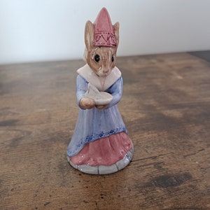 May include: A ceramic figurine of a rabbit wearing a pink and white hat and a blue and pink dress. The rabbit is holding a white plate in its paws.