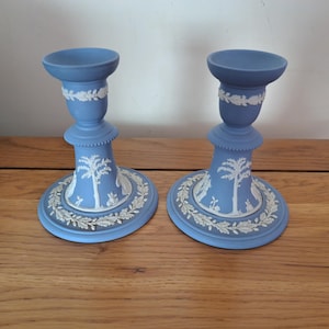 Può includere: Due candelabri blu in ceramica con disegni a rilievo bianchi. I candelabri presentano una base rotonda con una scena dettagliata, uno stelo centrale e una coppa superiore. Le basi misurano circa 12,7 cm di diametro.