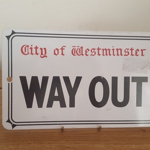 Może przedstawiać: Biały metalowy znak z czarnym napisem, na kt&oacute;rym widnieje "City of Westminster" w kolorze czerwonym i "WAY OUT" w kolorze czarnym. Znak ma czarną ramkę i dwa małe otwory u g&oacute;ry i na dole.