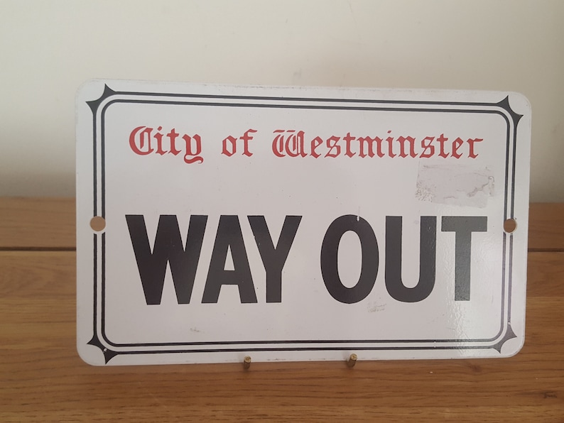 Może przedstawiać: Biały metalowy znak z czarnym napisem, na kt&oacute;rym widnieje "City of Westminster" w kolorze czerwonym i "WAY OUT" w kolorze czarnym. Znak ma czarną ramkę i dwa małe otwory u g&oacute;ry i na dole.