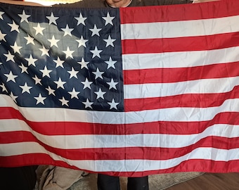 Può includere: Una persona che tiene una grande bandiera americana con strisce rosse e bianche e un campo blu con stelle bianche.