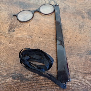 Op de afbeelding: Een zwarte, opvouwbare loep met een zwart lint. De loep heeft twee ronde lenzen.