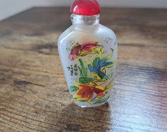 May include: A small, frosted glass bottle with a red stopper. The bottle is decorated with three colorful goldfish and Chinese characters.