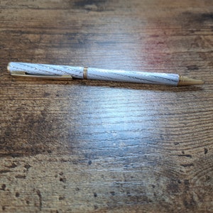 May include: A silver pen with a gold band and a white and gray patterned design.