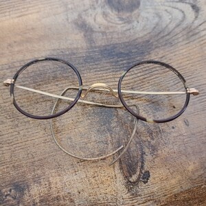 May include: Round, brown-rimmed glasses with gold metal arms and a gold nose bridge.