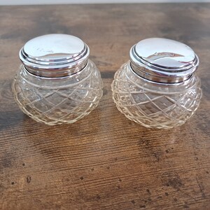 May include: Two clear glass jars with silver lids. The jars have a diamond pattern and the lids have a smooth, shiny finish.