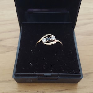 May include: A gold ring with three stones, two clear and one black, set in a twisted band.
