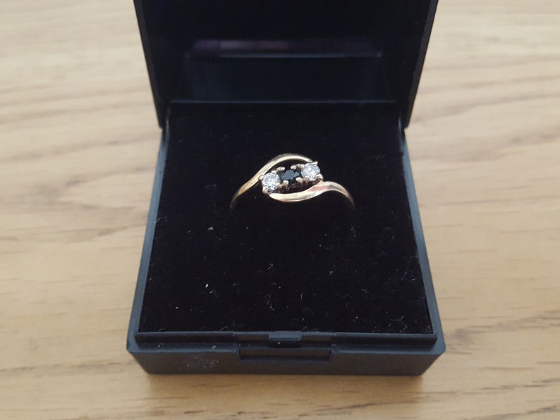 May include: A gold ring with three stones, two clear and one black, set in a twisted band.