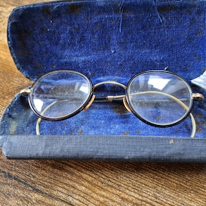 May include: A pair of round, black-rimmed glasses with gold accents, resting in a blue velvet lined case.