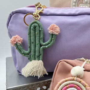May include: Two small lavender and peach colored zippered pouches with fabric tassels. The lavender pouch has a green and white cactus keychain attached. The peach pouch has a rainbow-colored yarn keychain with white pom-poms.