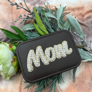 Könnte beinhalten: Eine schwarze Schmuckschatulle mit einem Perl- und Gold-Design "Mom".