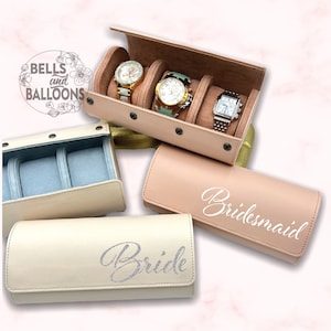 Könnte beinhalten: Eine Sammlung von Uhrenetuis und Reiseetuis in verschiedenen Farben. Ein Etui ist geöffnet und zeigt drei Uhren. Zwei Etuis sind mit "Bride" und "Bridesmaid" beschriftet. Die Etuis sind in Rosa-, Creme- und Goldtönen gehalten.