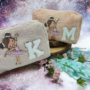 May include: Two beige zippered pouches with embroidered ballerina figures and glitter letters. The pouch on the left has a white K and the pouch on the right has a white M.