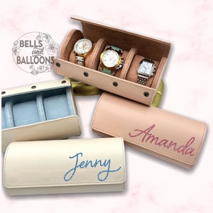 May include: Several watch cases in cream and light pink. One case is open, revealing three watches. Two closed cases feature the names "Jenny" and "Amanda" in glitter script. The cases are designed for watch storage.