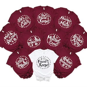 May include: Ten burgundy t-shirts with white text and graphics. The shirts feature various Harry Potter themed phrases, including "Maid of Mischief", "She's a Catch", "She Found a Keeper", "Mischief Maker", "Mischief Crew", "Witch of Honor", "Bridesmaid", "Bride's Army", "House Bachelorette", and "I Found a Keeper".