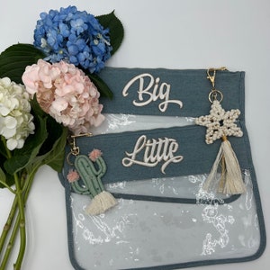 May include: Two denim zippered pouches with clear vinyl windows. The pouches are labelled "Big" and "Little". A gold key chain with a white star charm and tassel hangs from the top pouch.