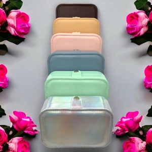 May include: Six stackable jewellery boxes in different colours, including brown, beige, pink, blue, green, and iridescent. The boxes are arranged vertically, with the brown box on top and the iridescent box at the bottom.