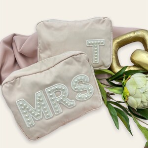 May include: Two pink zippered pouches with pearl-embellished letters. One pouch says "MRS" and the other says "T".