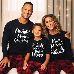 May include: Family matching pajama sets. The black long-sleeve shirts and t-shirt have white text that reads "Mischief Mode Activated", "Mischief Not Really Managed", and "Mom Manager of Mischief". The pajama pants are red and black plaid.
