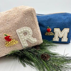 May include: Two cosmetic bags with the letters "R" and "M" on them. The bag with the letter "R" is beige and has a red apple with the words "Super Teacher" on it. The bag with the letter "M" is blue denim and has a red apple with the words "Super Teacher" on it.