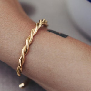 May include: A gold-toned twisted bangle bracelet. The bracelet is made of a thick, braided metal and has a simple, elegant design.
