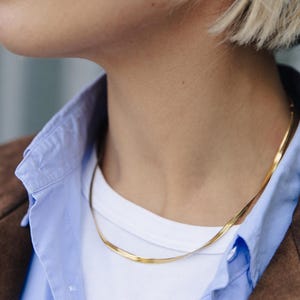 May include: A gold chain necklace worn on a person's neck. The chain is thin and has a delicate, slightly textured design.