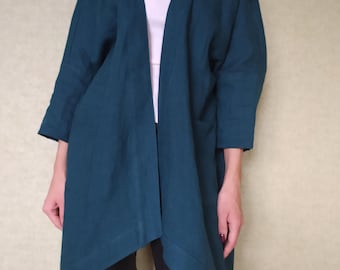 May include: A teal-colored linen jacket with a V-neck design and three-quarter sleeves. The jacket has a relaxed fit and features two front pockets. The model is wearing a white top underneath and black pants.