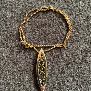 May include: A gold chain necklace with a silver pendant featuring a detailed, ornate design of swirling patterns.
