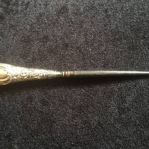 May include: A silver shoe horn with an ornate, engraved handle and a black metal hook.