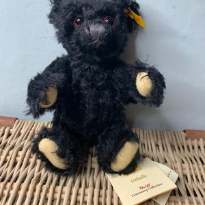 Puede incluir: Oso de peluche negro Steiff con ojos rojos y una etiqueta amarilla que dice "Steiff Centenary Collection Othello".