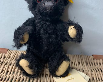 Puede incluir: Oso de peluche negro Steiff con ojos rojos y una etiqueta amarilla que dice "Steiff Centenary Collection Othello".