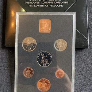 Könnte beinhalten: Ein Proof-Set britischer Münzen von 1971, präsentiert in einer transparenten Hülle. Das Set enthält verschiedene Nennwerte, wie 10-Pence- und 50-Pence-Münzen, sowie eine rechteckige Münze. Der Text auf der Hülle lautet: "THE UNITED KINGDOM ADOPTED A DECIMAL COINAGE SYSTEM ON 15TH FEBRUARY 1971".