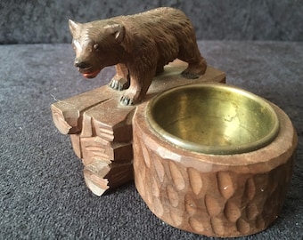 May include: A wooden bear figurine sits atop a carved wooden log base with a brass-lined ash tray. The bear is brown and has a black nose and eyes.