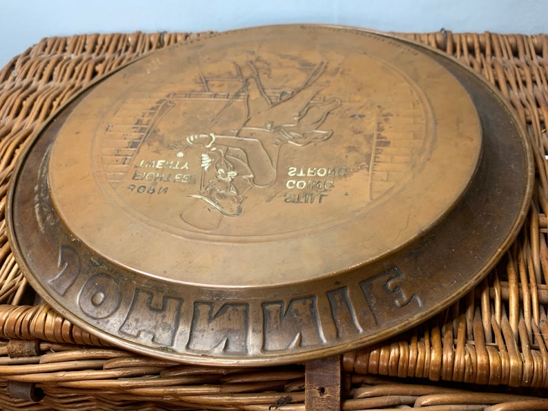 Puede incluir: Una bandeja redonda de servir de lat&oacute;n con una imagen en relieve de un deshollinador subiendo por una escalera. La bandeja tiene las palabras "Johnnie Walker" en relieve alrededor del borde y el texto "The Extra Strong Scotch Whisky" en el centro.