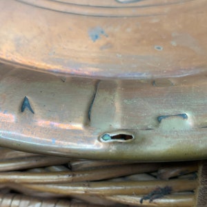 Puede incluir: Primer plano de la parte inferior de un plato de metal de color cobre con un peque&ntilde;o agujero en el centro. El plato tiene un patr&oacute;n decorativo alrededor del borde.