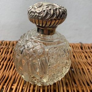 May include: A clear glass bottle with a cut glass design and a silver stopper. The stopper has a detailed floral design.