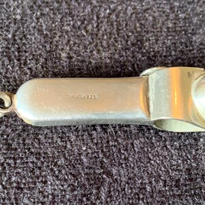 May include: A silver-colored,  sterling silver,  cigarette lighter with a hinged lid and a loop for attaching to a keychain.