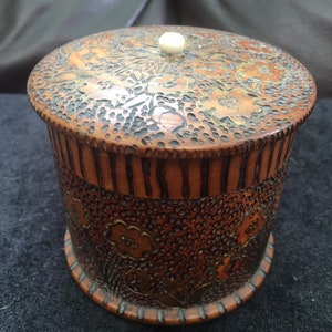 May include: A round wooden box with a carved floral design and a white knob on the lid.