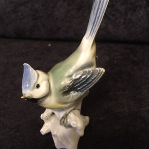 May include: A porcelain figurine of a bluebird perched on a branch. The bird is painted in shades of blue, green, and yellow, with black accents. The figurine is a vintage piece and is in good condition.