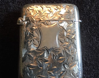 Op de afbeelding: Een zilveren luciferdoosje met een ingewikkeld bloemmotief. Het luciferdoosje heeft een scharnierend deksel en een klein slotje.