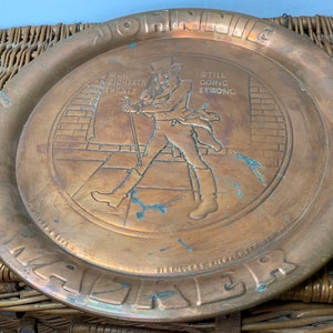 Puede incluir: Una bandeja redonda de lat&oacute;n con una imagen en relieve de un hombre caminando. La bandeja tiene las palabras "Johnnie Walker" y "Born 1820 Still Going Strong" alrededor del borde.