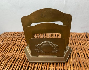 Puede incluir: Un portacartas de latón con un diseño decorativo que presenta un círculo y hojas. El portacartas tiene tres compartimentos para cartas.
