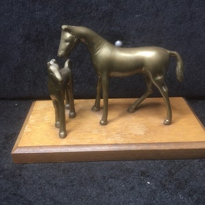 Peut inclure: Une sculpture en laiton d'un cheval et d'un poulain sur une base en bois. Le cheval est debout, la tête baissée, et le poulain est debout à côté de lui.