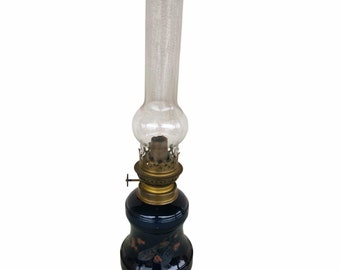 May include: A blue glass oil lamp with a clear glass chimney and brass accents. The lamp has a floral design painted on the base.