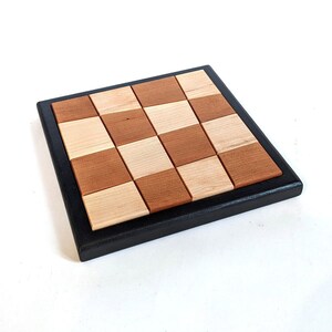 May include: A wooden game board with a black frame. The board is divided into 16 squares, alternating between light and dark wood.
