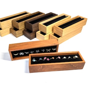 May include: A set of wooden ring and earring display boxes. The boxes are made of light and dark wood and have a velvet lining. The boxes are stacked on top of each other. The top box has a variety of rings and earrings displayed on the velvet lining.